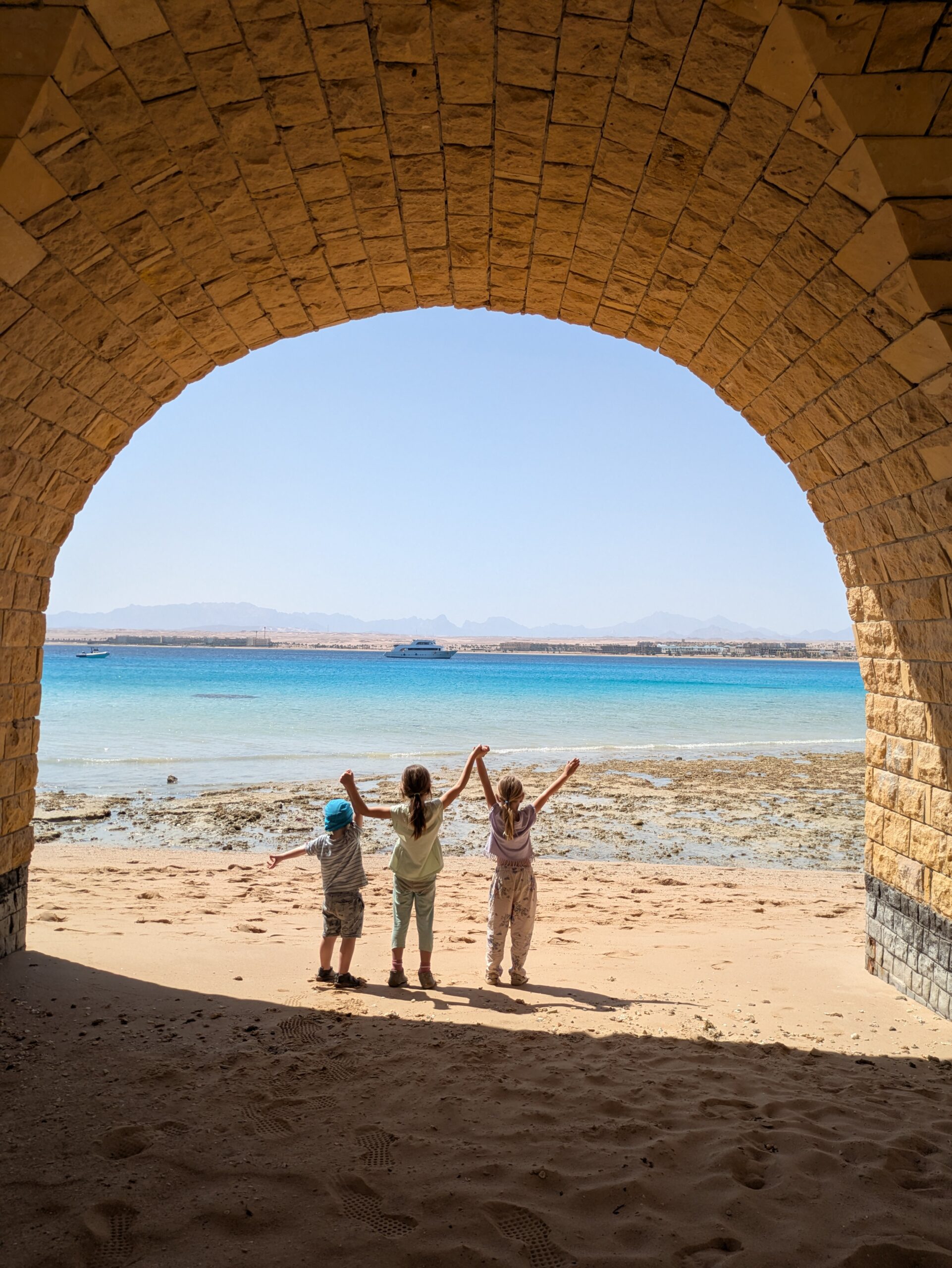L'image montre 3 enfants les bras levé devant la Mer Rouge lors d'un voyage en Egypte